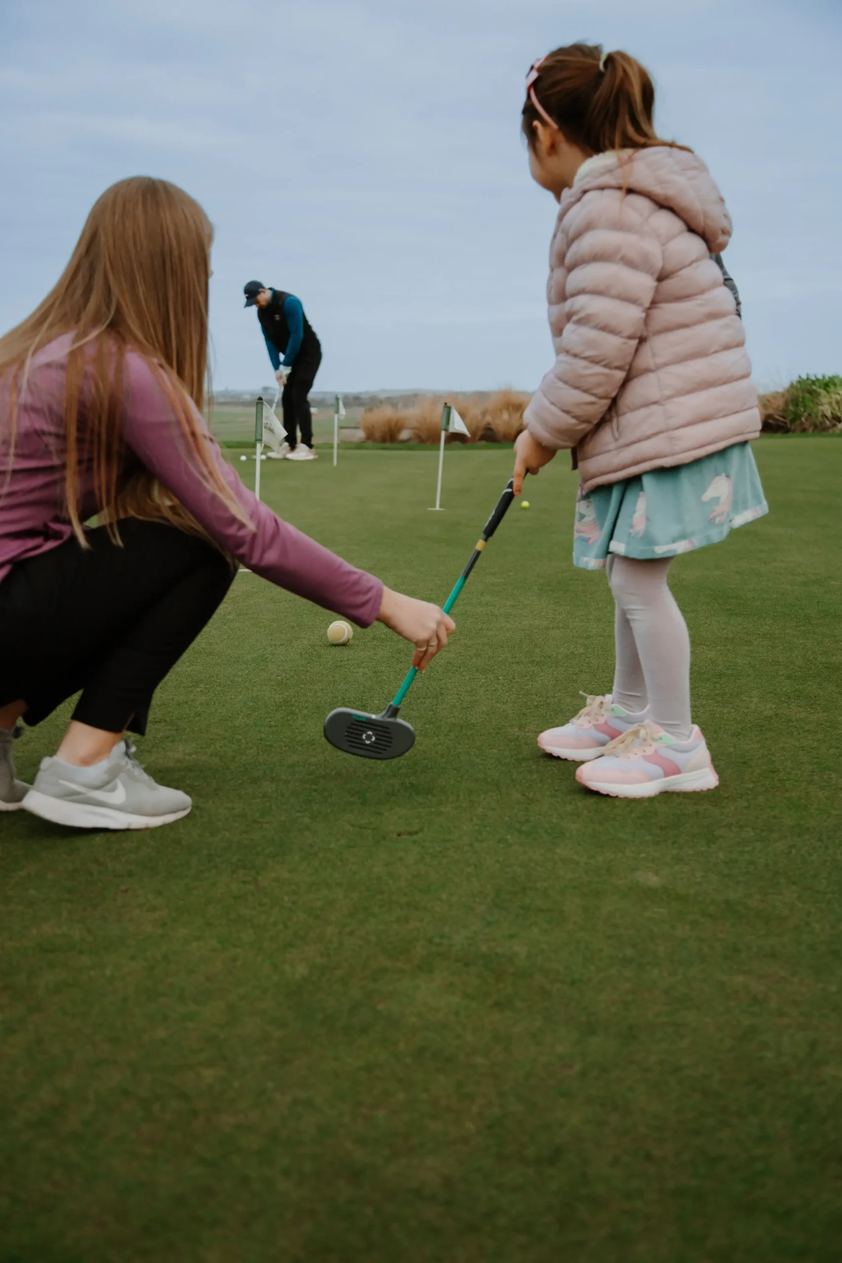 Child learning to play golf with guidance on the green, promoting golf lessons and golf lessons Cornwall.